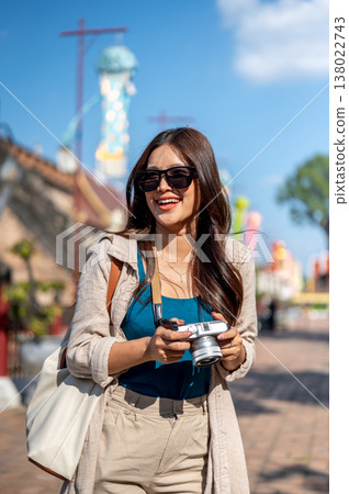 Woman wearings sunglasses holding camera looking around standing aside pagoda in buddhist temple. 138022743