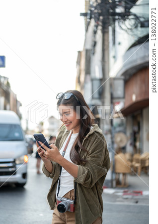 Happy asian woman holding and looking at phone while standing walking by street road in local town. 138022771