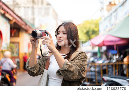 Pretty asian woman holding camera taking picture standing or walking in local street market of town. Pretty asian woman holding camera taking picture standing or walking in local street market of town. 138022778