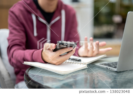 Close up of man student freelancer looking confused at smartphone over book and laptop at cafe table Close up of man student freelancer looking confused at smartphone over book and laptop at cafe table 138023048