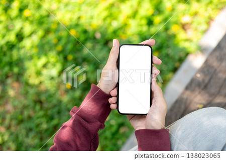 Top view close up of a man holding white screen phone with both hands while sitting at garden park. Top view close up of a man holding white screen phone with both hands while sitting at garden park. 138023065