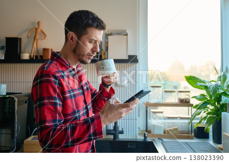 Man in pajamas drinking coffee and using smartphone at home 138023390