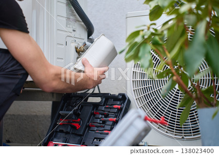 Technician servicing outdoor heat pump unit at residential house 138023400