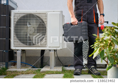 Technician with toolbox standing near outdoor heat pump unit Technician with toolbox standing near outdoor heat pump unit 138023402