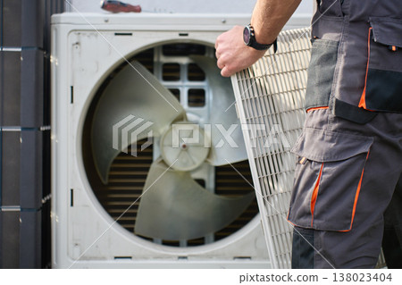 Technician removing cover grille from outdoor heat pump unit 138023404