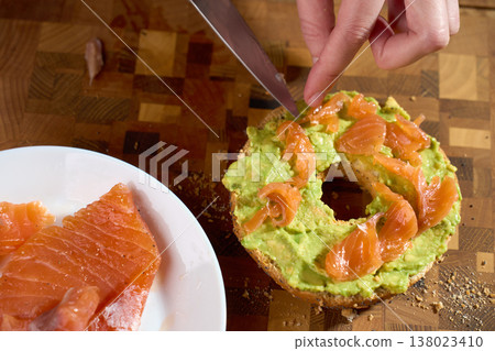Hand adding smoked salmon to avocado bagel during healthy breakfast prep 138023410