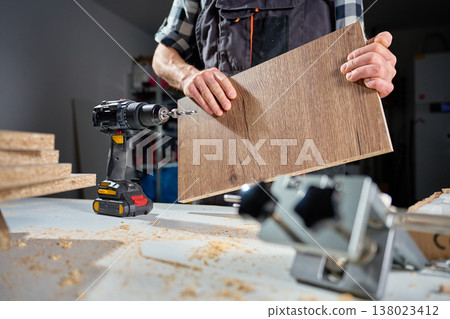 Carpenter holding wood panel near cordless drill in workshop 138023412