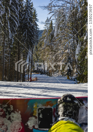 Snowboarders ride down a trail in a forest during a sunny winter day Snowboarders ride down a trail in a forest during a sunny winter day 138023697