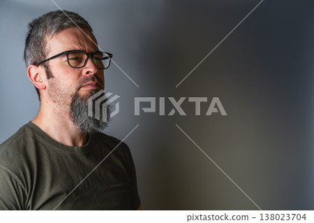 Man with glasses stands in profile with serious expression in studio 138023704