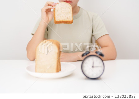 Happy smiling woman eating whole wheat bread with alarm clock. concept of intermittent fasting, IF, meal timing, and choosing healthy carbohydrates for a balanced diet and weight loss management Happy smiling woman eating whole wheat bread with alarm clock. concept of intermittent fasting, IF, meal timing, and choosing healthy carbohydrates for a balanced diet and weight loss management 138023852