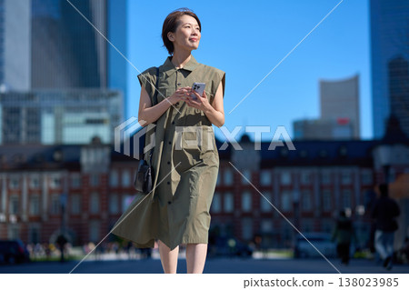 一位三十多歲的日本女性手持智慧型手機走在街上。 138023985
