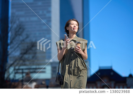 A Japanese woman in her 30s walking down the street with her smartphone in her hand. 138023988