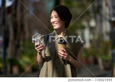 A Japanese woman in her 30s walking down the street with her smartphone in her hand. 138023993