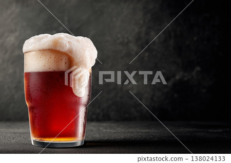 A glass of red beer with rich foam shown on a dark background, concept of refreshment and craft brewing A glass of red beer with rich foam shown on a dark background, concept of refreshment and craft brewing 138024133