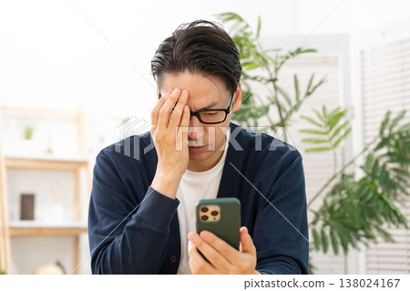 一名男子看著他的智慧型手機，心事重重；他感到震驚。 138024167