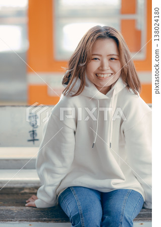 Portrait of a woman in her 20s sitting on a train station bench. Portrait of a woman in her 20s sitting on a train station bench. 138024180