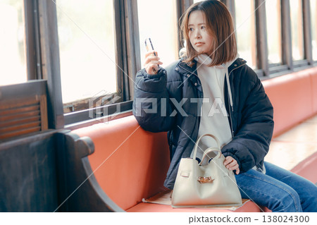一位二十多歲的女性在火車上使用智慧型手機的肖像。 一位二十多歲的女性在火車上使用智慧型手機的肖像。 138024300