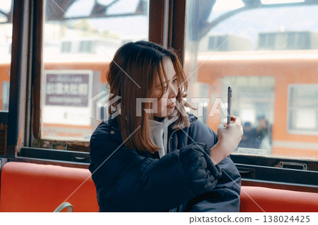 Portrait of a woman in her 20s using her smartphone on a train. Portrait of a woman in her 20s using her smartphone on a train. 138024425