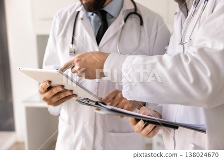 Closeup doctors discussing patient information on electronic tablet on clipboard Closeup doctors discussing patient information on electronic tablet on clipboard 138024670