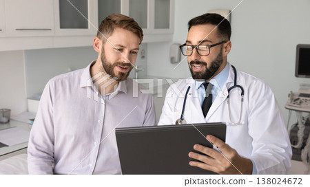 Positive smiling doctor holding paper clipboard speaking to happy patient Positive smiling doctor holding paper clipboard speaking to happy patient 138024672