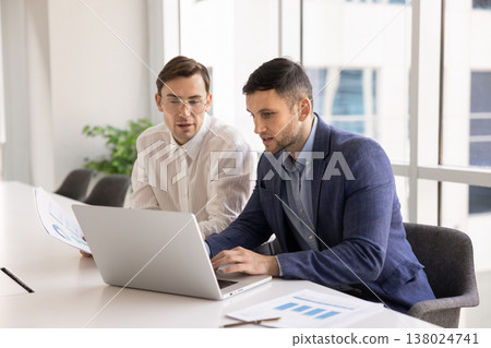 Two focused young businessmen sitting at conference desk using laptop 138024741