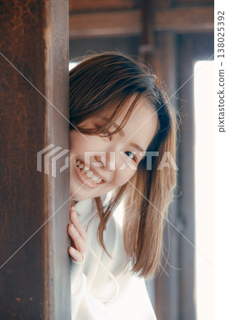 A woman in her twenties smiles as she sticks her head out of the door of a retro train. 138025392