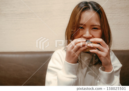 一位二十多歲的微笑的女子正在吃飯團。 138025501