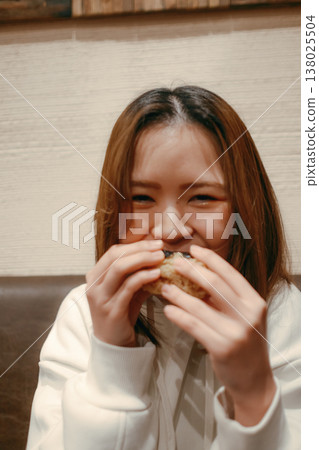 A smiling woman in her 20s eating a rice ball. 138025504