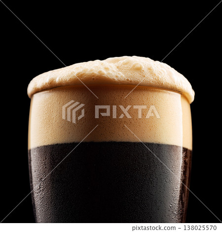 Foamy dark stout beer in a pint glass with creamy foam head, isolated on black background, concept of refreshment and taste Foamy dark stout beer in a pint glass with creamy foam head, isolated on black background, concept of refreshment and taste 138025570