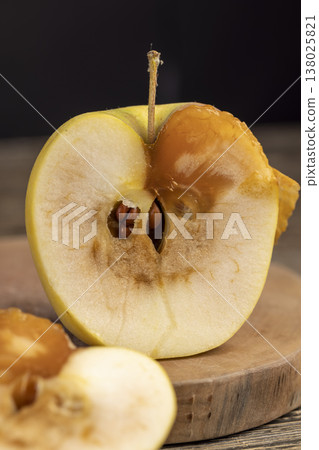a cut apple with a large orange spot during rotting, one rotting apple on a black wooden table made of pine wood cut into two halves, the apple is rotten inside 138025821