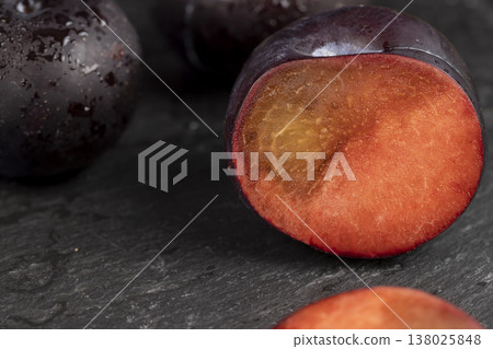 sliced black fresh juicy plums on the kitchen table, some beautiful pure black plums on the table, plum with juicy sweet flesh cut into pieces 138025848