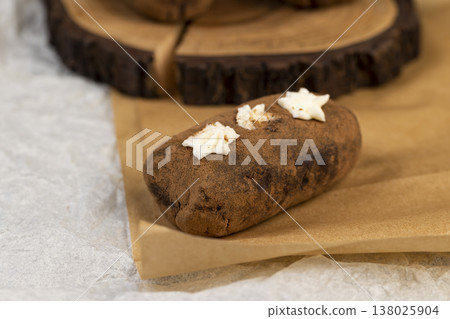 a black potato cake lies on a serving board and paper, a sweet classic cake made from butter and a large amount of cocoa mixed with sponge cake and cognac a black potato cake lies on a serving board and paper, a sweet classic cake made from butter and a large amount of cocoa mixed with sponge cake and cognac 138025904