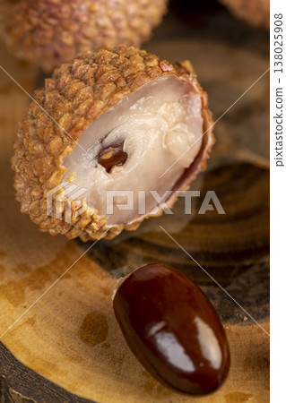 open ripe red lychees cut into pieces on a wooden table, ripe lychee fruits with cut pink tough peel, lychee close up open ripe red lychees cut into pieces on a wooden table, ripe lychee fruits with cut pink tough peel, lychee close up 138025908
