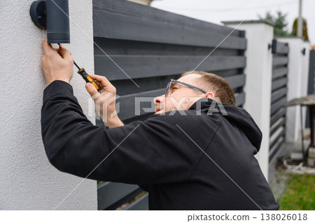 Man installing outdoor wall light with screwdriver 138026018