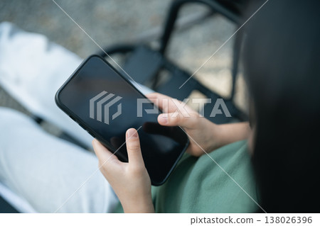 Close-up of a person holding a smartphone while sitting outdoors, showcasing a relaxed lifestyle with a focus on modern technology and communication. Close-up of a person holding a smartphone while sitting outdoors, showcasing a relaxed lifestyle with a focus on modern technology and communication. 138026396