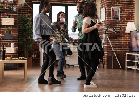 Different cultures, ethnicities people group dancing together in circle at center house living room. Friends, partners drinking wine, enjoying friendship, partnership at house party. 138027153