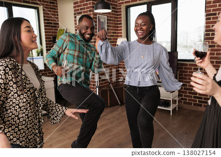 Young adult african american woman dancing, smiling amidst a different ethnicities, nationalities people group, laughing, drinking wine at gathering friends living room apartment. 138027154