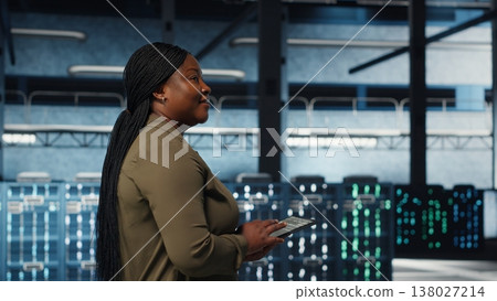 Smiling data center technician using tablet to manage software updates for system stability. Upbeat IT expert in server room configuring infrastructure with device for optimum performance, camera B 138027214