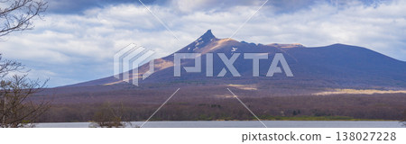 A panoramic view capturing the spring scenery of Mount Komagatake in Hokkaido, with light and shadow falling on the slopes and trees along the lakeshore (Nanae Town, Southern Hokkaido). A panoramic view capturing the spring scenery of Mount Komagatake in Hokkaido, with light and shadow falling on the slopes and trees along the lakeshore (Nanae Town, Southern Hokkaido). 138027228