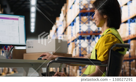 Asian man in wheelchair processing orders and preparing the boxes for distribution in fulfillment center, wears hi vis vest in e commerce logistics facility. Retail fast delivery. Camera B. 138027291
