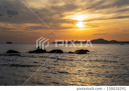 Seaside Fisherman Sitting on Rocks at Sunset 138028291