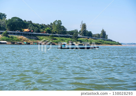 Long Boat Cruising Along River with Village on Shore 138028293