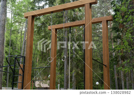 Outdoor Wooden Fitness Frame With Gymnastic Rings And Climbing Rope In Forest Park Outdoor Wooden Fitness Frame With Gymnastic Rings And Climbing Rope In Forest Park 138028982