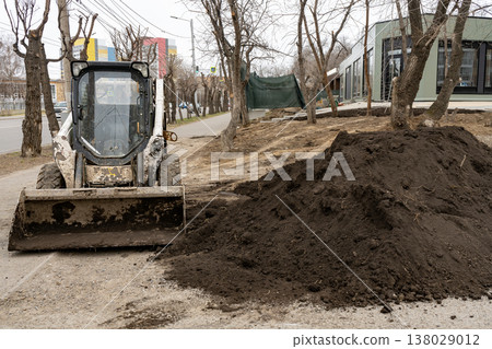 A small bulldozer on wheels unloads soil for a lawn. A small bulldozer on wheels unloads soil for a lawn. 138029012
