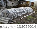 Plastic Covered Garden Bed Near Log Shed With Compost Pile in Rural Backyard 138029014