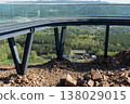 Glass Observation Deck With Steel Supports Overlooking Forest Valley, Rocky Slope and Distant Mountains 138029015