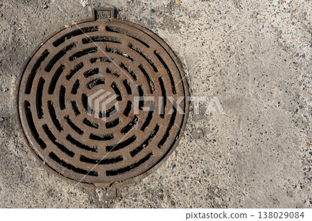 Rusty Round Manhole Cover With Concentric Grate Pattern In Weathered Concrete Pavement Rusty Round Manhole Cover With Concentric Grate Pattern In Weathered Concrete Pavement 138029084