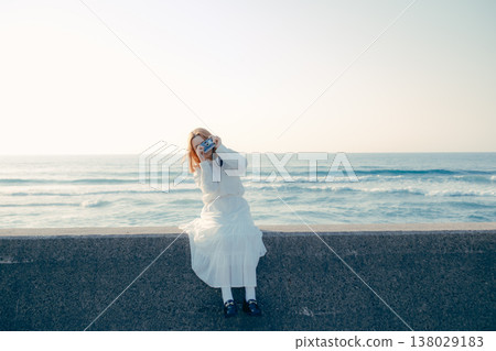 一位年輕女子拿著相機坐在沙灘上。 138029183