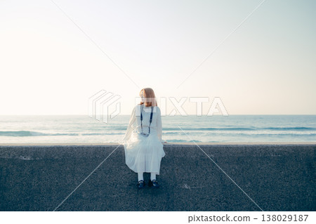 一位年輕女子拿著相機坐在沙灘上。 138029187