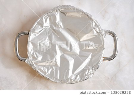 Pork rib chop covered in foil resting on a round metal pan in a kitchen setting 138029238